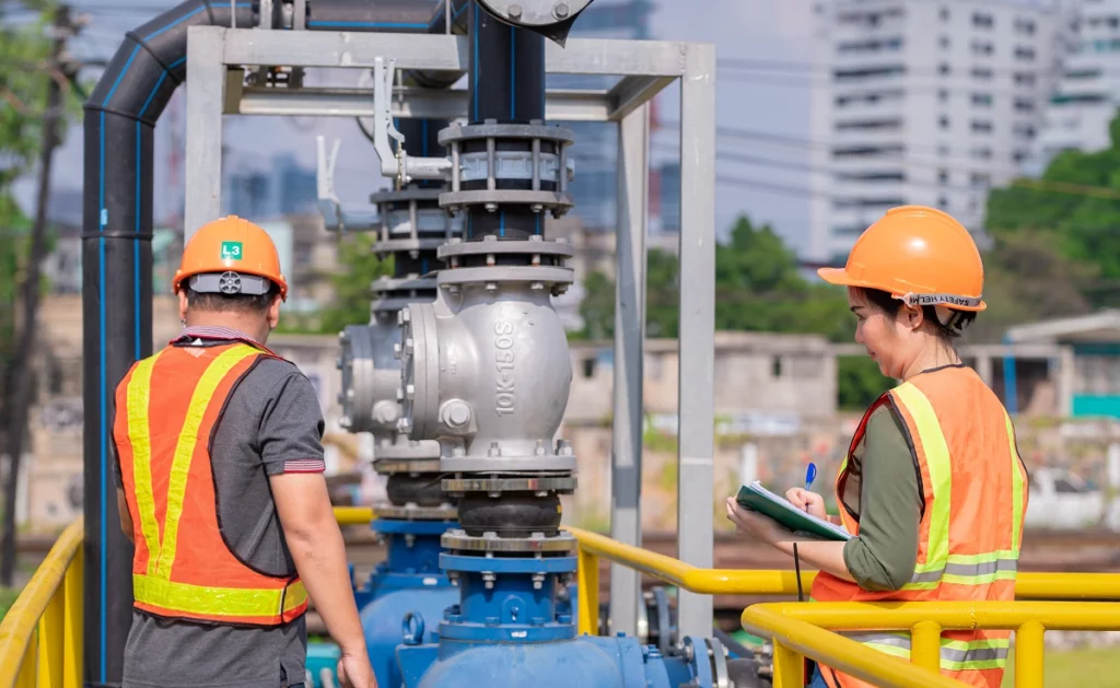 Maintenance team conducting an outdoor inspection of industrial pump valves and piping, documenting observations on site