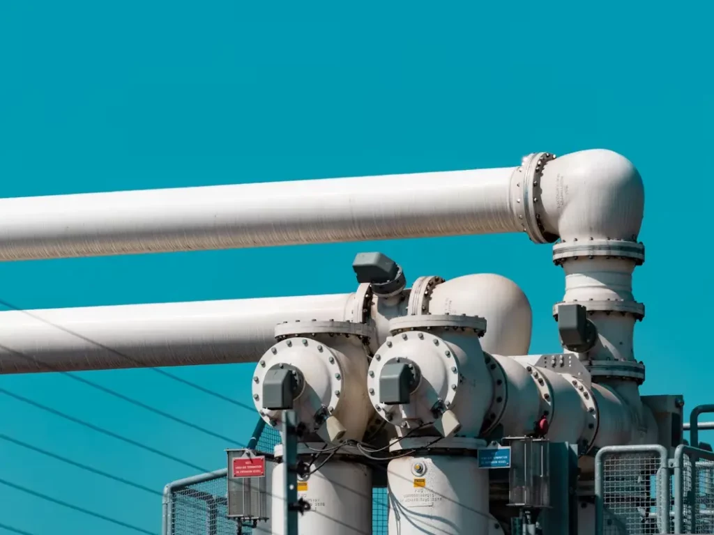 White industrial pipes and pump connections against a bright blue sky, showing heavy-duty infrastructure